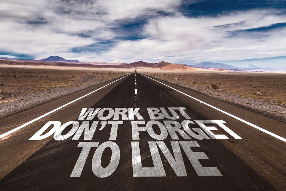 Long desert road painted with "work but don't forget to live"